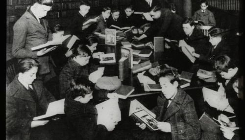 Work with schools : after a book talk, showing boys gathered around table reading, ca. 1920s, The New York Public Library Digital Collections