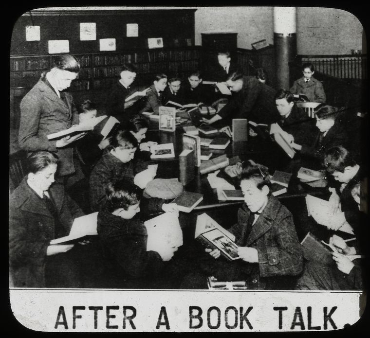 Work with schools : after a book talk, showing boys gathered around table reading, ca. 1920s, The New York Public Library Digital Collections